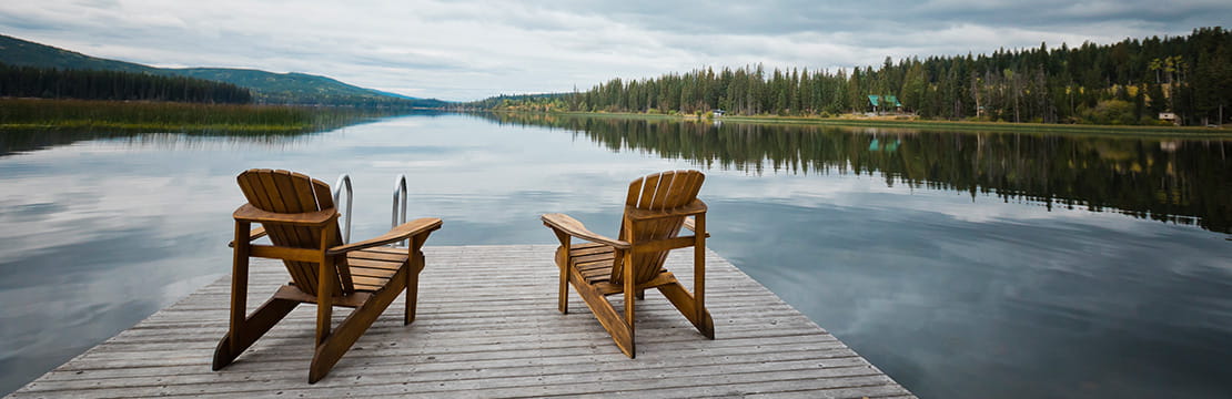 A peaceful lakeside dock with two chairs, symbolizing the lifestyle and planning considerations of moving to a new state in retirement.